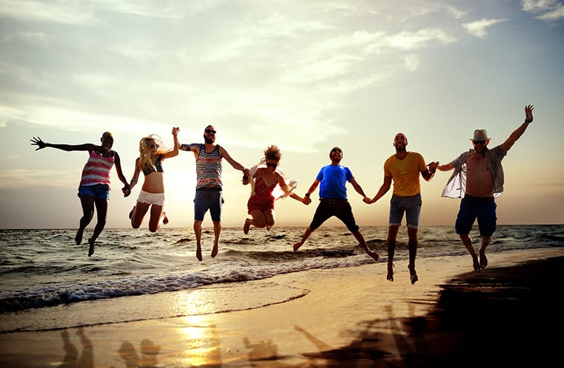 A group of people jumping in the air on top of a beach.