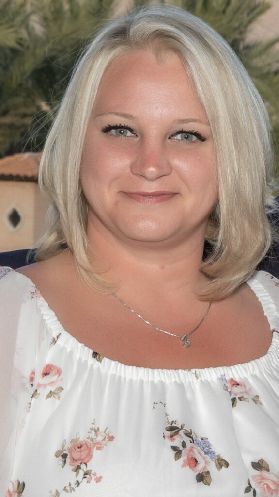 A woman with blonde hair wearing white and smiling.